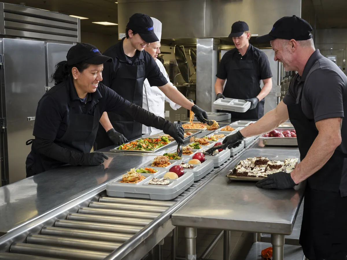 Workers in assembly line making trays of food in commercial kitchen