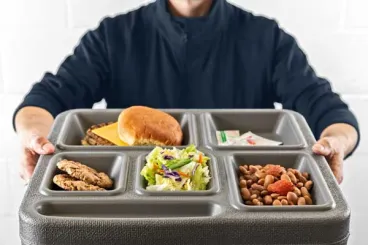 Person holding plastic food tray with cheeseburger, cookies, salad and baked beans