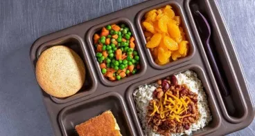 Overhead head shot of food tray with rice & beans, corn bread, mixed vegetables, oranges and cookie