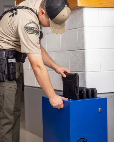 A sheriff officer is placing electronic devices into a blue mobile cart in a jail.